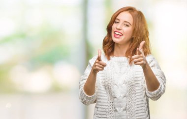 İzole arka plan kış kazak işaret parmakları için fotoğraf makinesi ile mutlu ve komik yüz giyen genç güzel kadın. İyi enerji ve vibes.