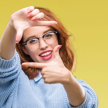 İzole arka plan elle yapma çerçeve ve parmakları ile mutlu yüz gülümseyen kış kazak giyen genç güzel kadın. Yaratıcılık ve Fotoğrafçılık kavramı.