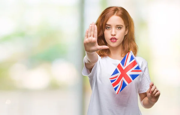 年轻美丽的妇女持有英国国旗在孤立的背景与张开手做停止标志认真和自信的表达 防御姿态 — 图库照片