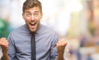 Genç yakışıklı iş adamı izole arka plan kutlama üzerinde şaşırttı ve başarı için kaldırdı kollarını açarak hayret ve gözleri açık. Kazanan kavramı.