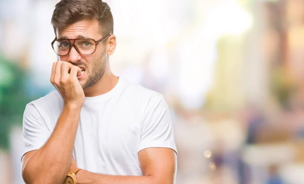 年轻英俊的男子戴着眼镜在孤立的背景下 看着压力和紧张的嘴咬指甲的手 焦虑问题 — 图库照片