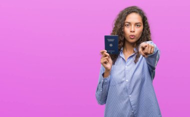 Genç İspanyol kadın holding pasaport, Almanya ile kamera ve size parmakla, el işareti, pozitif ve kendinden emin bir jest ön