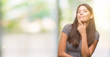 Çapraz kollar ve çeneme kaldırdı el ile gülümseme ile kameraya kendine güvenen arayan genç güzel İspanyol kadın. Pozitif düşünce.