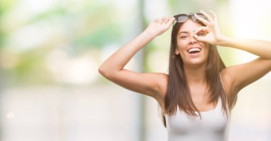 El gülümseyen, ok jest yapıyor genç güzel İspanyol giyen güneş gözlükleri göz parmakları ile mutlu yüz üzerinden seyir.