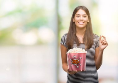 Bir gülen surat konumu olan patlamış mısır yemek ve diş gösterilen kendine güvenen bir gülümsemeyle gülümseyerek genç güzel İspanyol