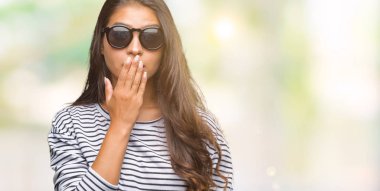 Genç güzel Arap kadın üzerinde güneş gözlüğü takıyor arka plan ağız hata için elleriyle kapsayan şok izole. Gizli kavramı.