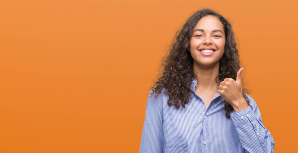 Young hispanic business woman doing happy thumbs up gesture with hand. Approving expression looking at the camera with showing success.