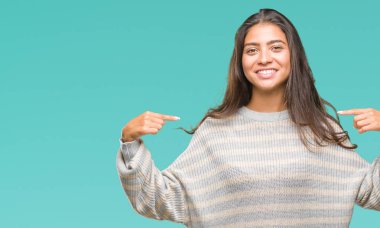 Yüzünde gülümseme ile kendinden emin görünüyorsun, kendini gururlu ve mutlu parmakları ile işaret izole arka plan üzerinde kış kazak giyen genç güzel Arap kadın.