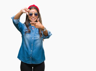 Genç güzel Arap kadın elle yapma çerçeve ve parmakları ile mutlu yüz gülümseyen izole arka plan üzerinde güneş gözlüğü takıyor. Yaratıcılık ve Fotoğrafçılık kavramı.
