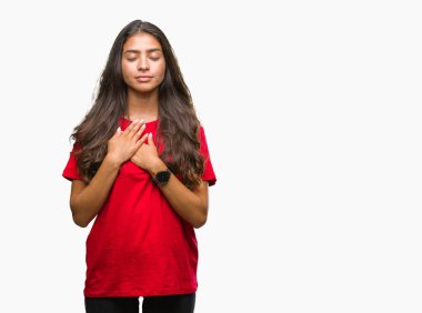 Eller genç güzel Arap kadın ile gülümseyen izole arka plan üzerinde kapalı gözler ve yüzünde minnettar jest ile göğüs üzerinde. Sağlık kavramı.