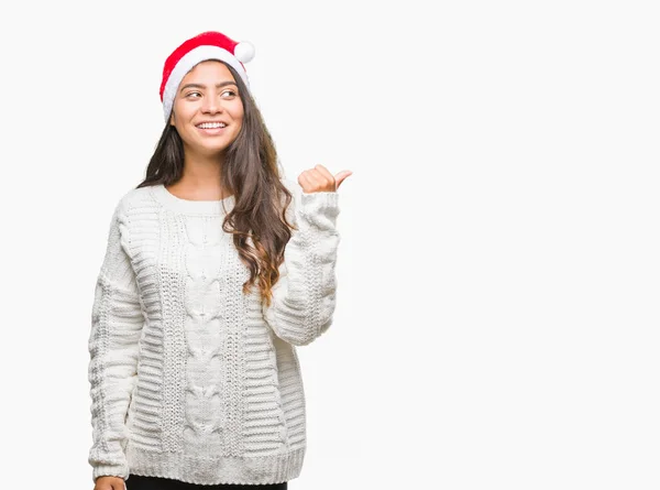 年轻的阿拉伯妇女戴着圣诞帽在孤立的背景微笑着快乐的脸看着 并指向侧面与拇指向上 — 图库照片