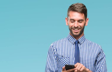 Genç atlatmışsınız adam manifatura izole arka plan üzerinde duran ve diş gösterilen kendine güvenen bir gülümsemeyle gülümseyerek mutlu bir yüz ile Smartphone kullanarak ileti gönderme