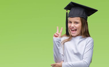 Genç güzel kız mutlu yüz zafer işareti yaparken kameraya göz kırpıyor ile gülümseyen izole arka plan üzerinde yüksek lisans şapkası. İki numaralı.