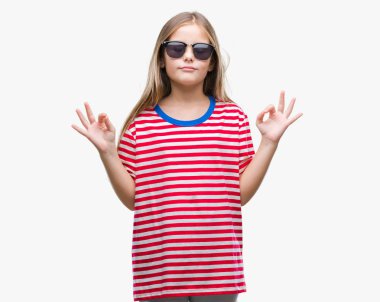 Genç güzel kız giyiyor güneş gözlüğü izole arka plan üzerinde dinlenmek ve gülümseyen gözlerle kapalı parmak jestle meditasyon yapıyor. Yoga kavramı.