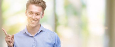 Genç yakışıklı sarışın adam el ve parmak ile tarafına işaret çok mutlu Smartphone kullanarak