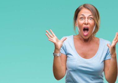 Orta yaş üst düzey İspanyol kadın deli kutluyor arka plan izole ve başarı için kaldırdı kollarını açarak hayrete ve heyecanlı çığlık gözleri açık. Kazanan kavramı