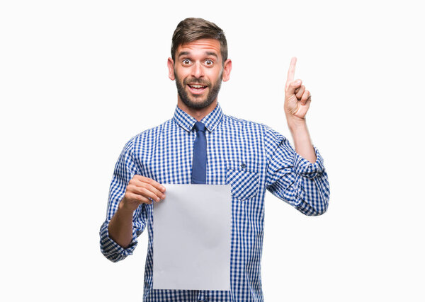 Young handsome man holding blank paper over isolated background surprised with an idea or question pointing finger with happy face, number one