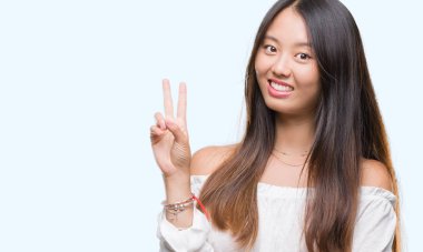 Genç Asyalı kadın mutlu yüz zafer işareti yaparken kameraya göz kırpıyor ile gülümseyen izole arka plan üzerinde. İki numaralı.