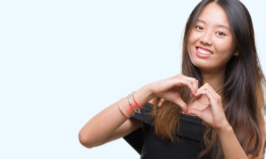 Genç Asyalı kadın kalp simgesi ve elleriyle şekil gösterilen aşık gülümseyen izole arka plan üzerinde. Romantik kavramı.