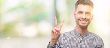 Zafer işareti yapıyor parmak gösterilen kamera seyir gülümseyen genç hipster adam. İki numaralı.