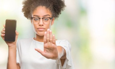 Genç güzel afro Amerikan gösteren smartphone ekran açık eliyle dur işareti ile ciddi ve kendine güvenen ifade, savunma jest yapıyor izole arka plan üzerinde