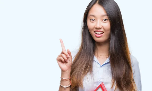 年轻的亚洲妇女真实的状态代理持有房子孤立的背景惊讶的想法或问题指着一个快乐的脸 — 图库照片