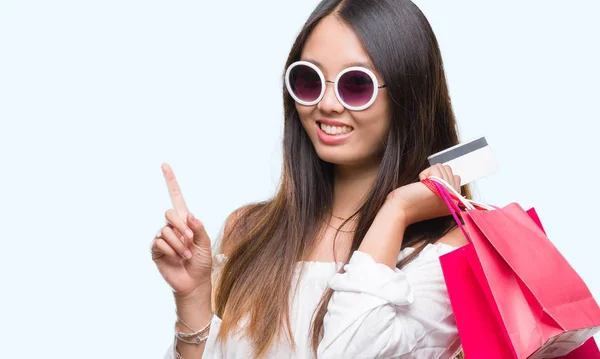 幸せそうな顔 ナンバーワンのアイデアや質問ポインティング指と分離の背景の上販売の買い物袋を保持している若いアジア女性を驚かせた — ストック写真