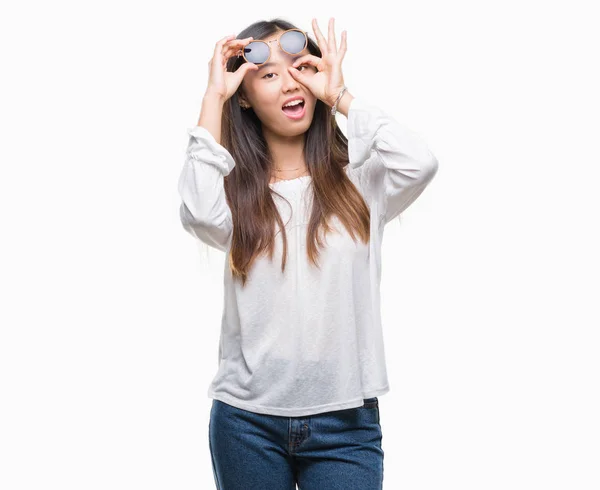 年轻的亚洲妇女戴着太阳镜在孤立的背景下做 手势用手微笑 眼睛看通过手指与愉快的面孔 — 图库照片
