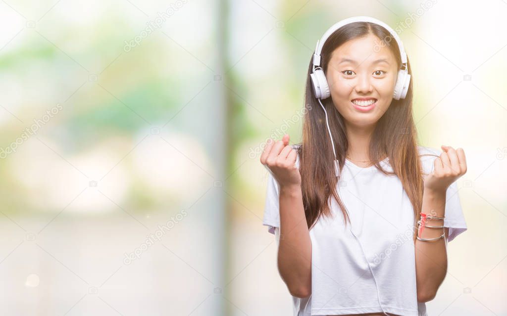 Young asian woman listening to music wearing headphones isolated background screaming proud and celebrating victory and success very excited, cheering emotion