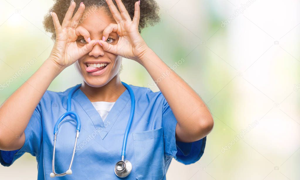 Young afro american doctor woman over isolated background doing ok gesture like binoculars sticking tongue out, eyes looking through fingers. Crazy expression.