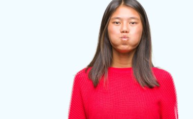 Komik surat ile yanakları şişirme izole arka plan üzerinde kış kazak giyen genç Asyalı kadın. Ağız ile hava, deli ifade şişirilmiş.