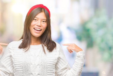 Yüzünde gülümseme ile kendinden emin görünüyorsun, kendini gururlu ve mutlu parmakları ile işaret izole arka plan üzerinde kış kazak giyen genç Asyalı kadın.