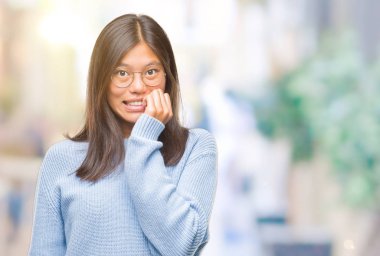 Stresli ve gergin elle çivi ısırma ağzına bakarak izole arka plan üzerinde kış kazak giyen genç Asyalı kadın. Anksiyete sorunu.