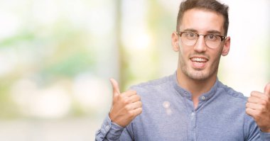 El ile pozitif jest yapıyor gözlük başarı işareti giyiyor zarif yakışıklı genç gülümseyen ve mutlu yaşasın. Neşeli bir ifadeyle, kazanan jest kameraya bakıyor.