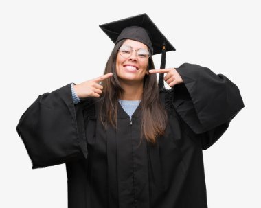 Kap ve kendinden emin gösterilen ve işaret parmakları diş ve ağız ile gülümseyen üniforma giyen genç İspanyol kadın mezun oldu. Sağlık kavramı.