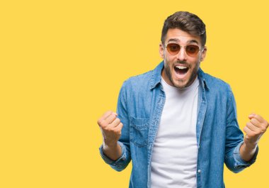 Yakışıklı delikanlı izole arka plan kutlama üzerinde güneş gözlüğü takıyor şaşırttı ve başarı için kaldırdı kollarını açarak hayret ve gözleri açık. Kazanan kavramı.