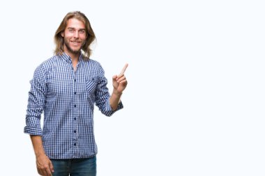 Kameraya bakarak yan el ve parmak ile işaret eden genç yakışıklı adam yüzünde kocaman bir gülümseme ile izole arka plan üzerinde uzun saçlı.