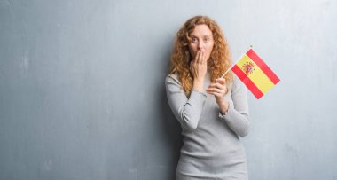 Hata, korku, sessizlik içinde gizli kavramı korkmuş ifade için utanç ile gri grunge duvar el ile İspanya kapak ağız bayrak tutan genç Kızıl saçlı kadın şok