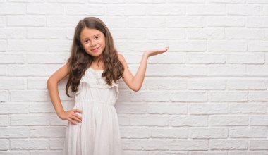 Beyaz tuğla duvar neşeli sunulması ve kameraya bakarak avucunun ile işaret gülümseyen genç İspanyol çocuk.