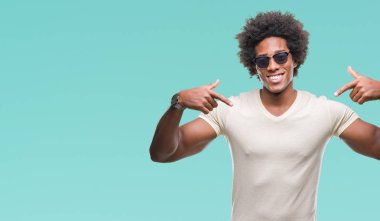 Yüzünde gülümseme ile kendinden emin görünüyorsun, kendini gururlu ve mutlu parmakları ile işaret izole arka plan üzerinde güneş gözlüğü takıyor Afro Amerikalı adam.