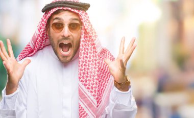 Keffiyeh üzerinde giyen genç yakışıklı adam deli kutluyor arka plan izole ve silah ile başarı için yükseltilmiş ve açık gözleri heyecanlı çığlık hayrete düşürdü. Kazanan kavramı