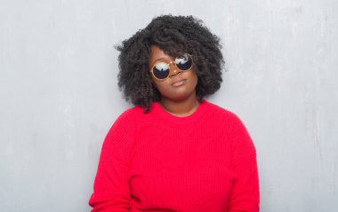 Genç Afro-Amerikan artı boyutu kadın yüzünde ciddi bir ifade ile retro güneş gözlüğü takıyor gri grunge duvarın üzerinden. Basit ve doğal kameraya bakıyor.