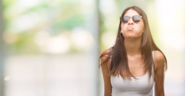 Genç güzel İspanyol komik surat ile yanakları şişirme güneş gözlüğü takıyor. Ağız ile hava, deli ifade şişirilmiş.