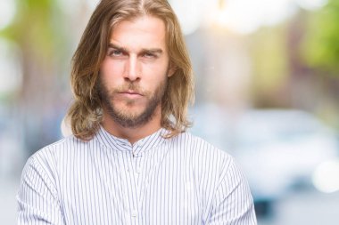 Yakışıklı delikanlı izole arka plan şüpheci ve sinir, onaylamayan ifade yüz çapraz kolları olan uzun saçlı. Negatif kişi.