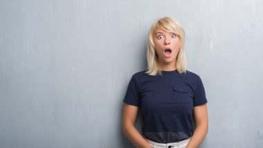 Grunge gri duvar bir sürpriz yüz, korkuyor ve heyecanlı korku ifadesi ile şok korkmuş yetişkin beyaz kadın
