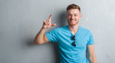 Genç Kızıl saçlı adam rahat kıyafet gülümseyen ve süre seyir ve kamera boyutu işaret parmaklarıyla yapıyor el ile kendinden emin eller gri grunge duvarın üzerinden. Ölçü kavramı.