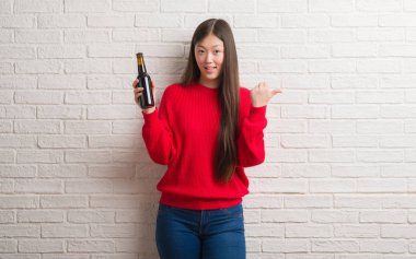 Genç Çinli kadın işaret ve başparmak kadar mutlu yüz gülümseyen tarafı ile gösterilen bira içme tuğla duvarın üzerinden