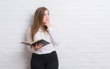 Okuma bir soru hakkında kitap ciddi bir yüz düşünme, çok karışık bir fikir beyaz tuğla duvardan duran genç yetişkin kadın