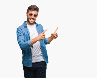 Yakışıklı delikanlı gülümseyen ve iki elleri ve parmakları ile tarafına işaret kamera bakarak izole arka plan üzerinde güneş gözlüğü takıyor.