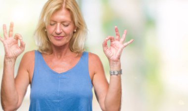 Orta yaş sarışın kadın izole arka plan üzerinde dinlenmek ve gülümseyen gözlerle parmak ile meditasyon jest yapıyor kapalı. Yoga kavramı.